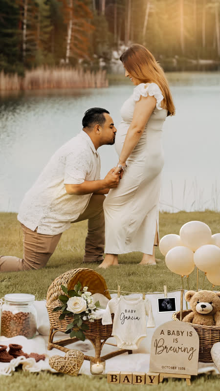 Father kissing belly by the lake with baby announcement setup